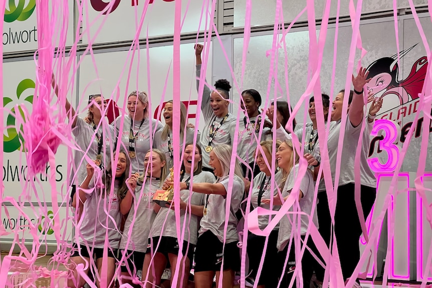 Thunderbirds players and coach pose for a photo with the trophy as pink streamers fall around them