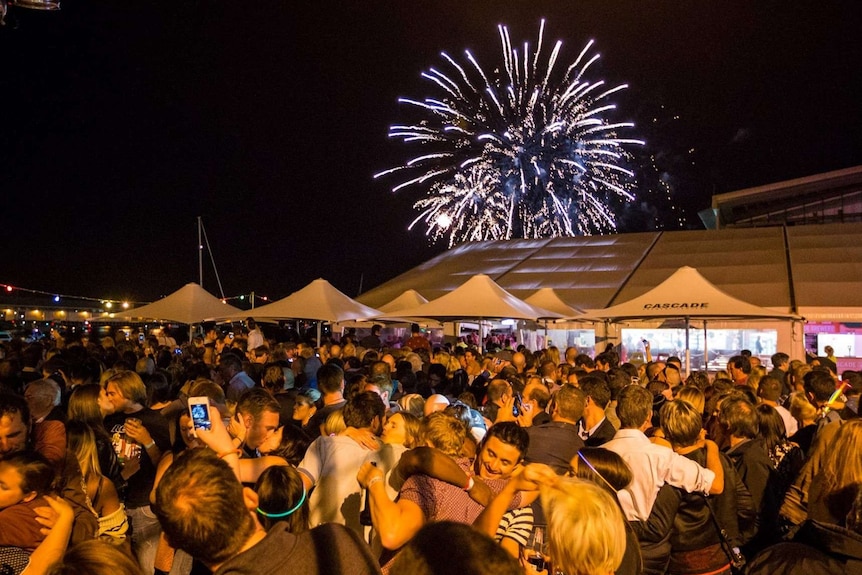 New Year's Eve crowd celebrates with fireworks overhead.