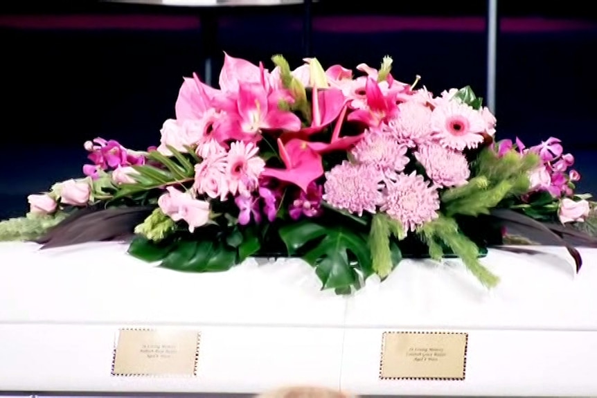 Pink flowers sit on top of a white coffin.