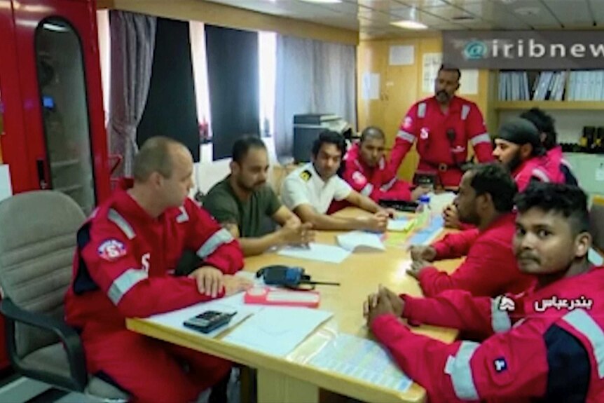 Crew members dressed in red uniforms sit around a table.