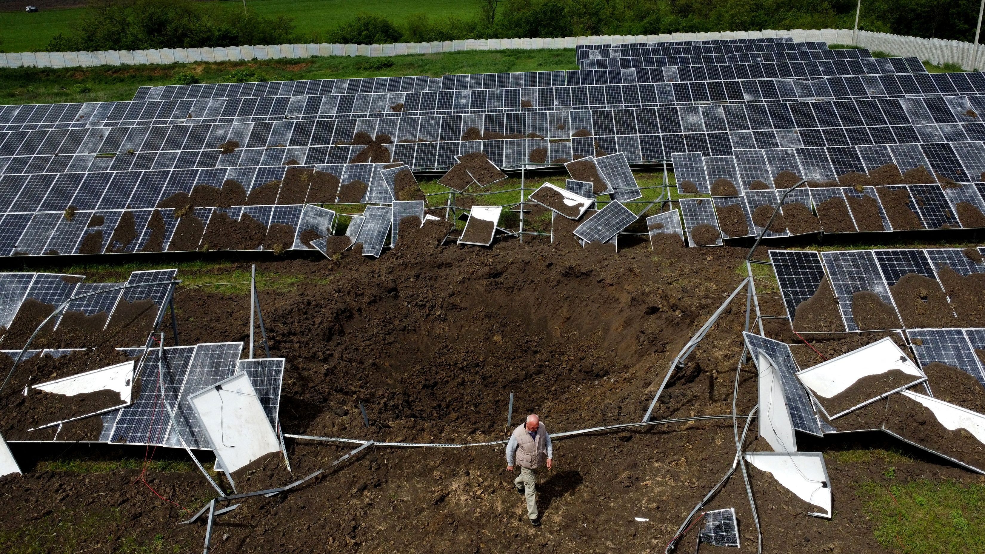 A middle-aged man walks over a large crater in the dirt amid solar panels on a solar farm.
