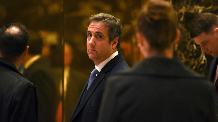 Michael Cohen in a suit looking back at the camera, with a neutral expression