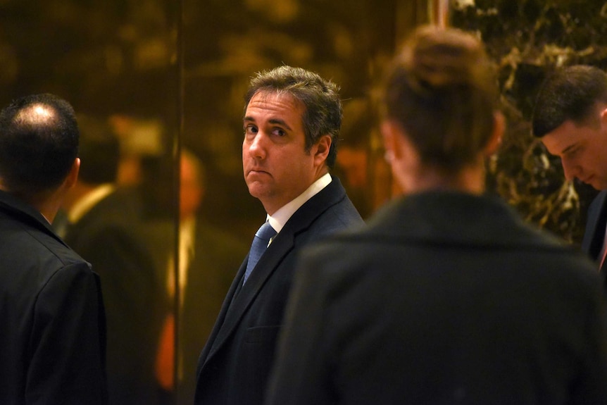 Michael Cohen in a suit looking back at the camera, with a neutral expression