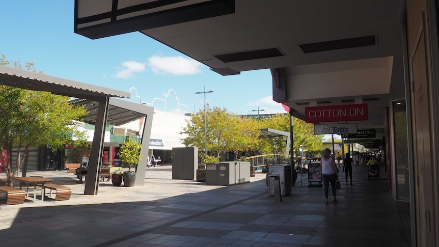 an empty pedestrian shopping strip with a row of shopfronts and a set of tables and chairs