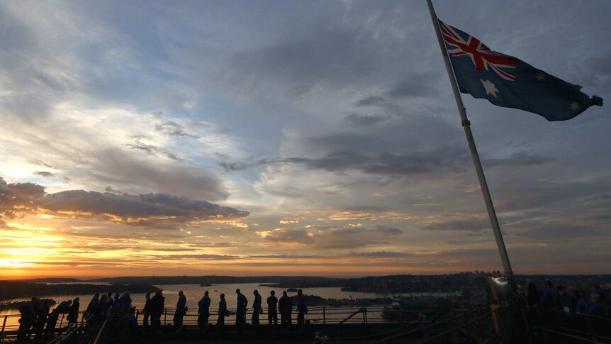 Australian flag and peoples silhouetted on top of Sydney Harbour Bridge.
