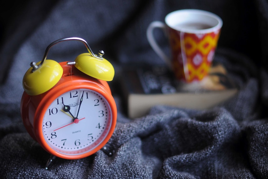An alarm clock sits next to a book and a mug.