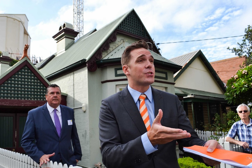 The auctioneer, a young man in a suit, spruiking the house for sale on auction day