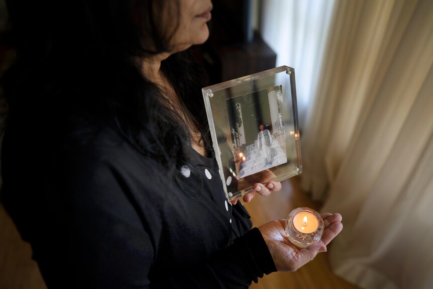 Woman holding a photo of her brother (whose face is blurred) and a tealight candle.