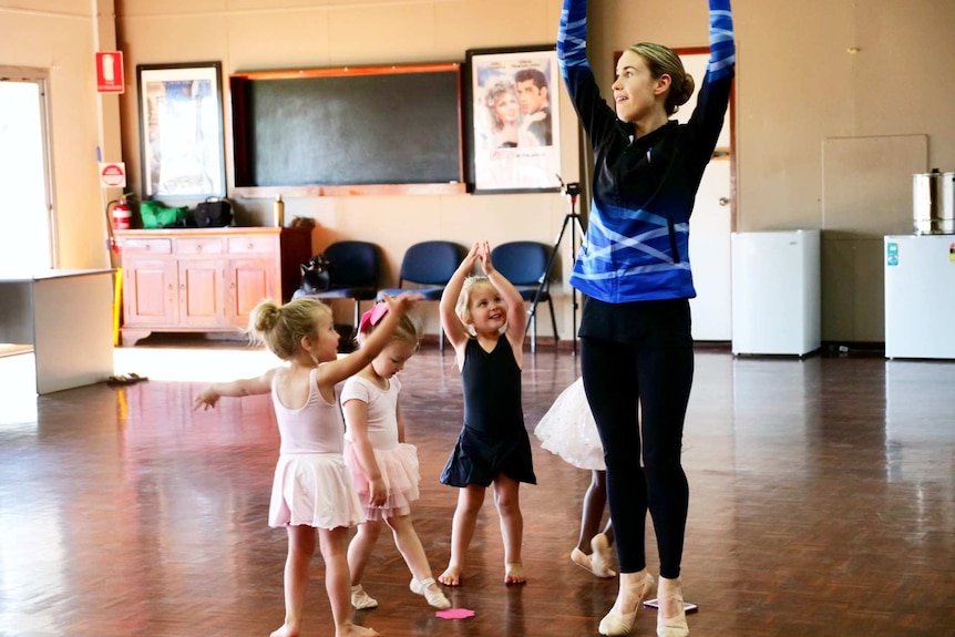 A young woman teaching four little girls dressed in ballet costumes how to twirl.