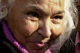 A woman with white hair smiling, while looking away from the camera.