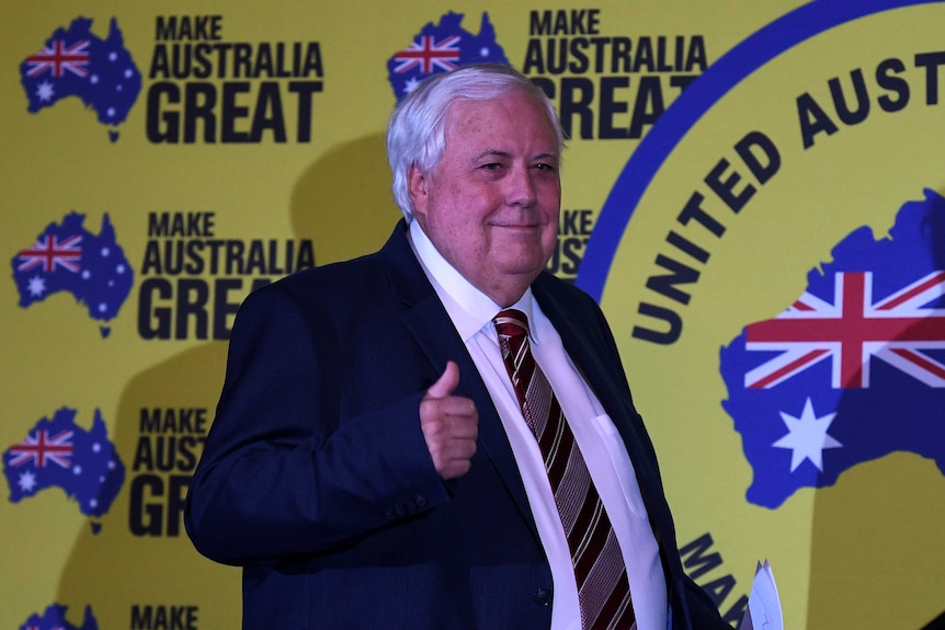 Mr Palmer pulls a "thumbs up" and smiles in front of signs that say "make Australia great".