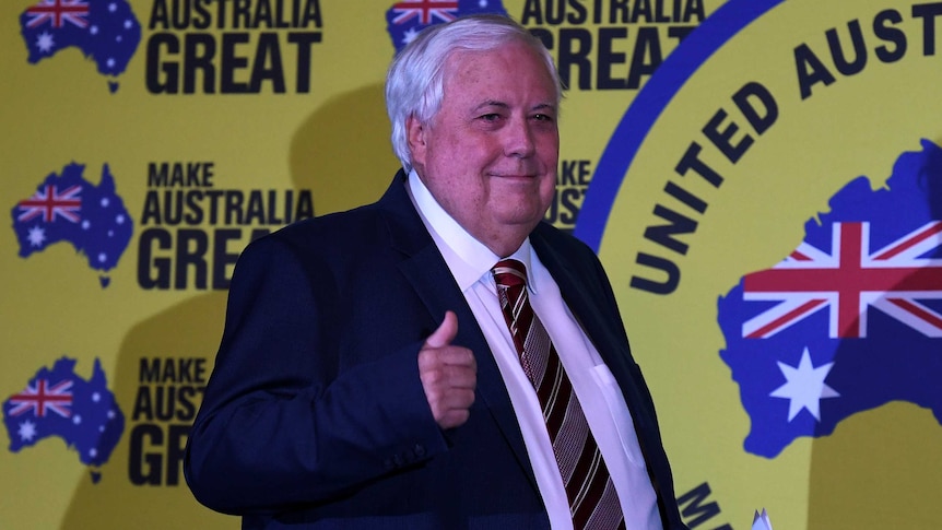 Mr Palmer pulls a "thumbs up" and smiles in front of signs that say "make Australia great".