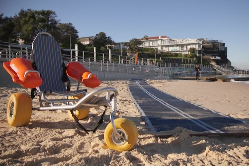 A modified wheelchair and beach mat sit on the sand at Bondi Beach