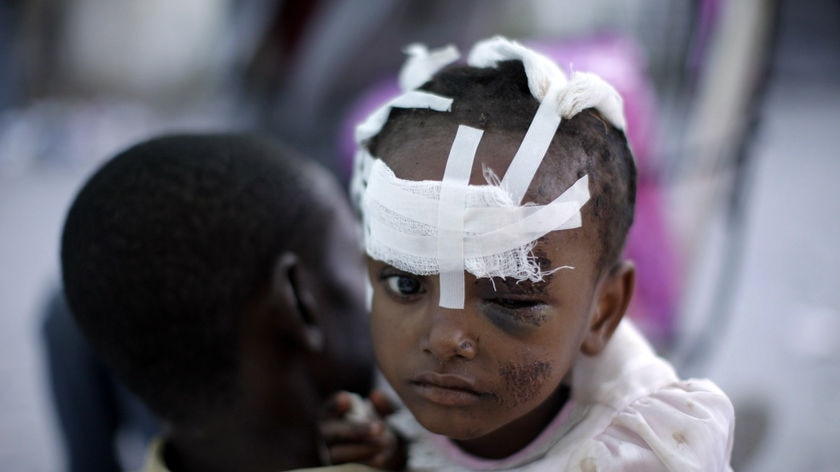 An injured girl is carried by her mother at a makeshift hospital on a street in Port-au-Prince