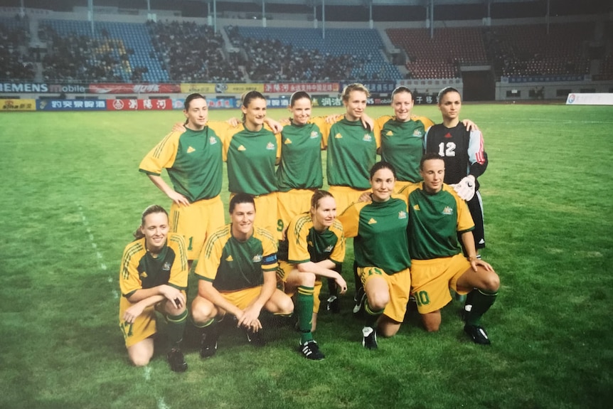 A women's soccer team wearing green and yellow poses for a photo before a game