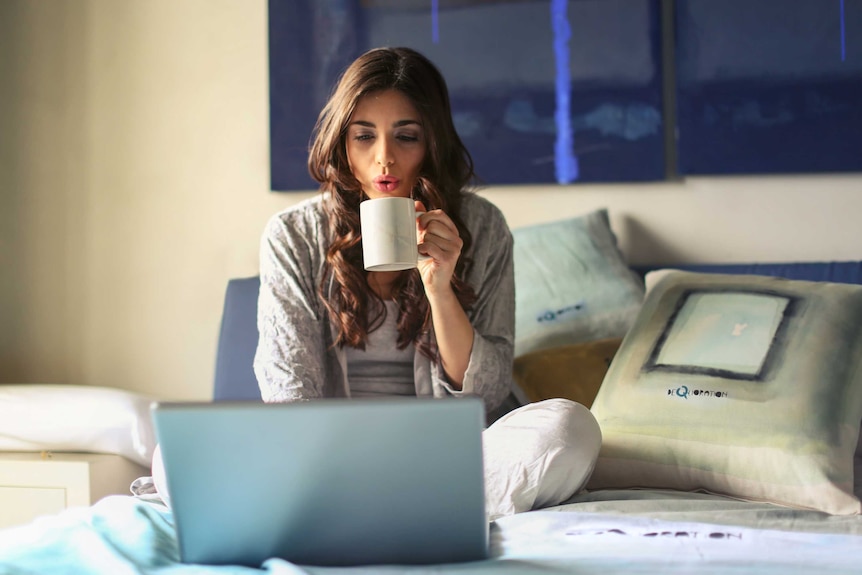 A woman sits in bed working on a laptop