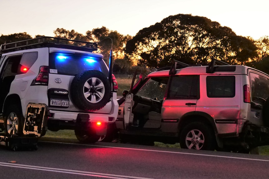 A white police 4WD with blue and red lights parked next to a gold, dented 4WD with doors open on the verge 