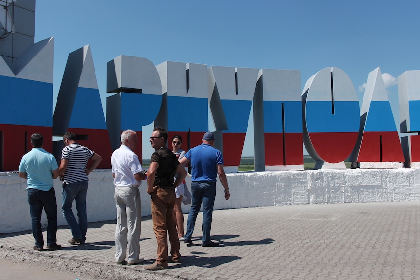 People stand near the name of the city of Mariupol written in Russian and painted in the colours of the Russian national flag 