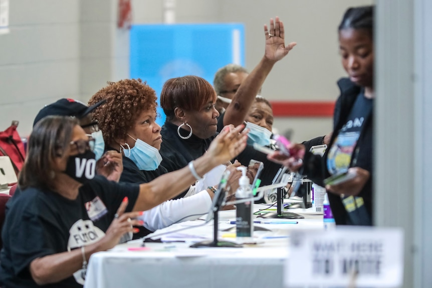 volunteers check people's ID at a desk as they line up to vote in georgia's senate runoff election