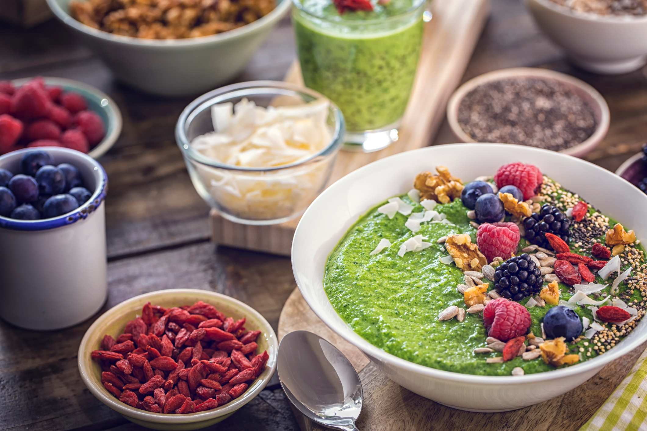 Um smoothie verde de café da manhã em uma tigela coberto com "superalimentos" como chia, quinoa, goji berries, frutas frescas e sementes de girassol.