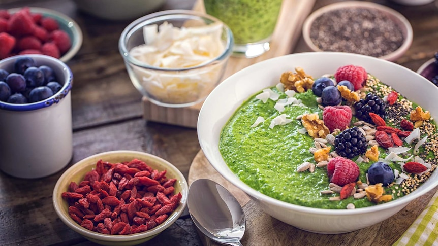 A green breakfast smoothie in bowl topped with "superfoods" like chia, quinoa, goji berries, fresh berries and sunflower seeds.