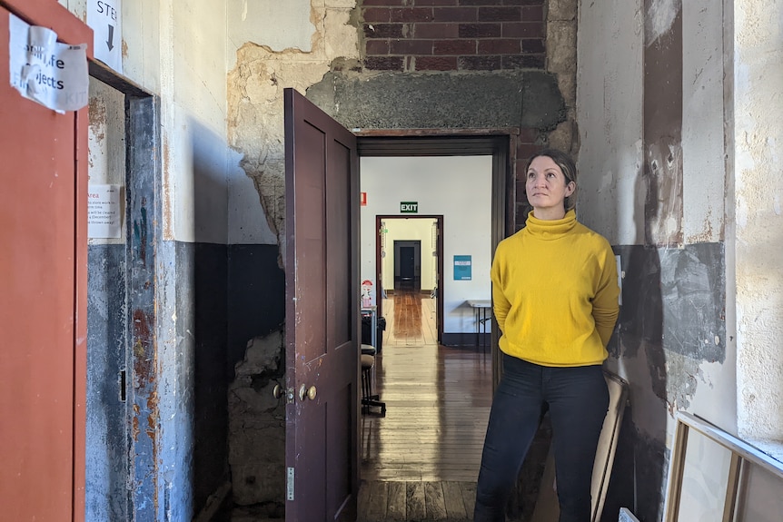 Anna Reece stands in doorway in front of a long hallway with exposed walls.