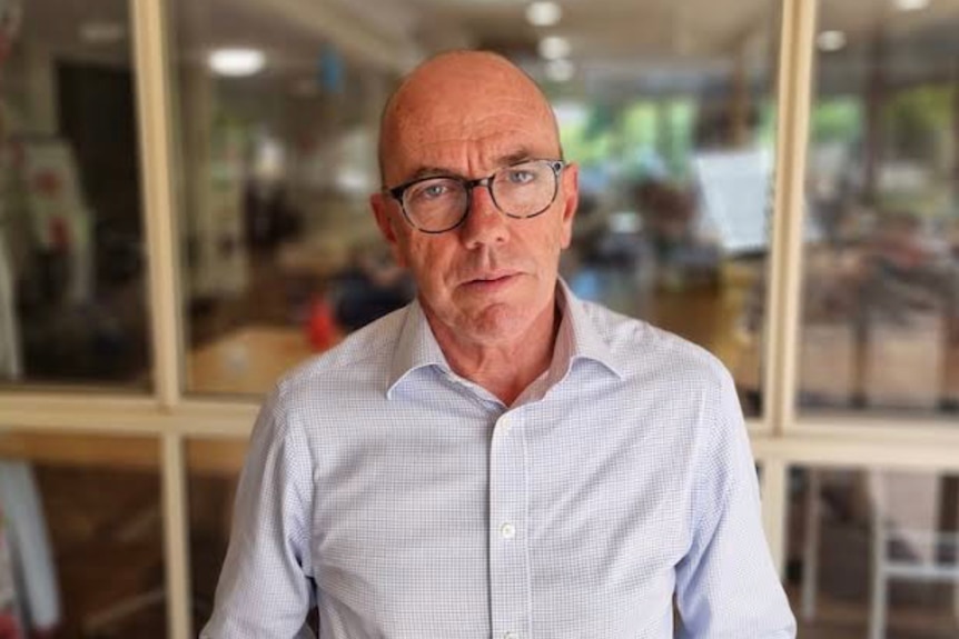 A portrait of a bald man wearing a button down shirt and glasses