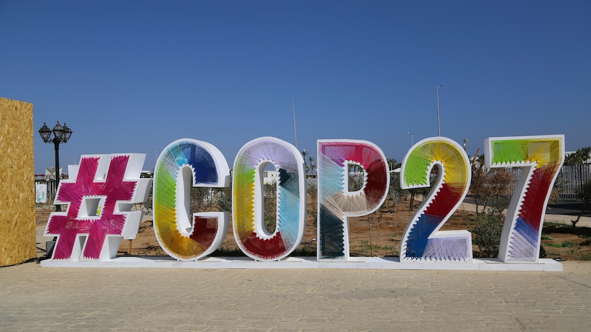 Colourful sign that says "#COP27" in front of blue sky.