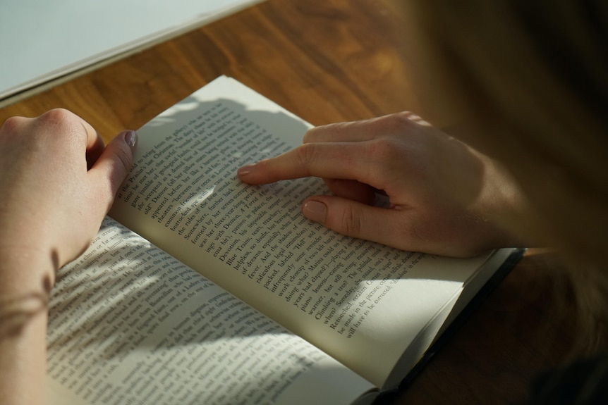 A person uses a finger to follow along the line reading a novel