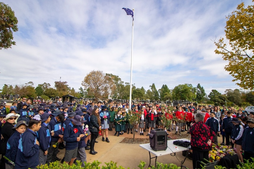 A crowd of school students gather underneath a flag pole at the Griffith Cemetery