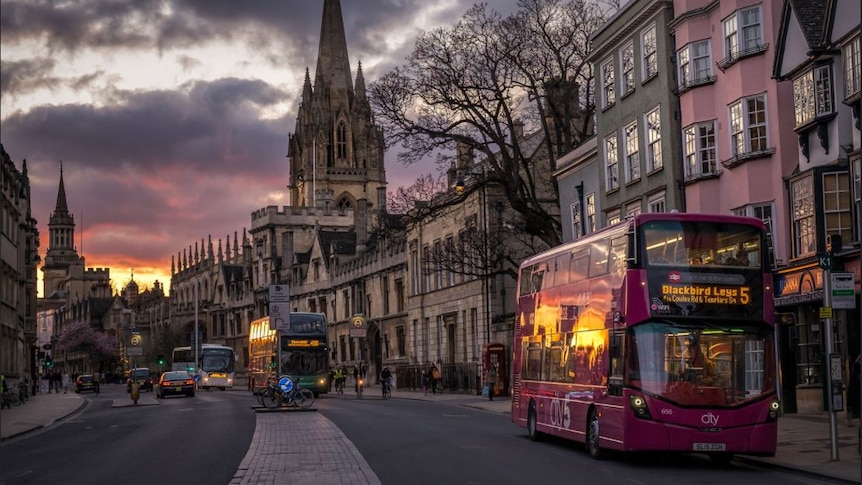 Buses line High Street, Oxford at sunset.