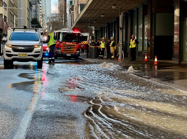 Water flows on the street outside a courthouse, with a white truck and fire truck and emergency services on scene.