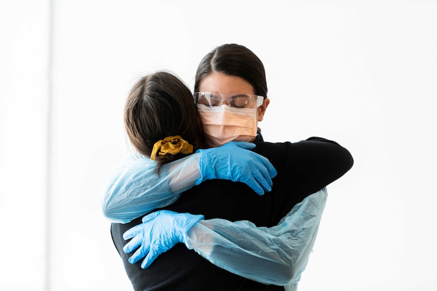 A woman in PPE (artist Merinda Davies) hugs a woman in casual clothes in a piece of performance art by Davies