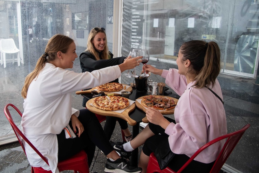 Women cheers over pizzas at a restaurant outside