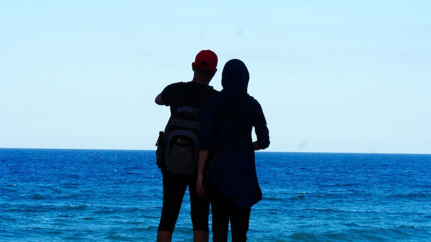 Two people stand in front of a beautiful blue ocean.