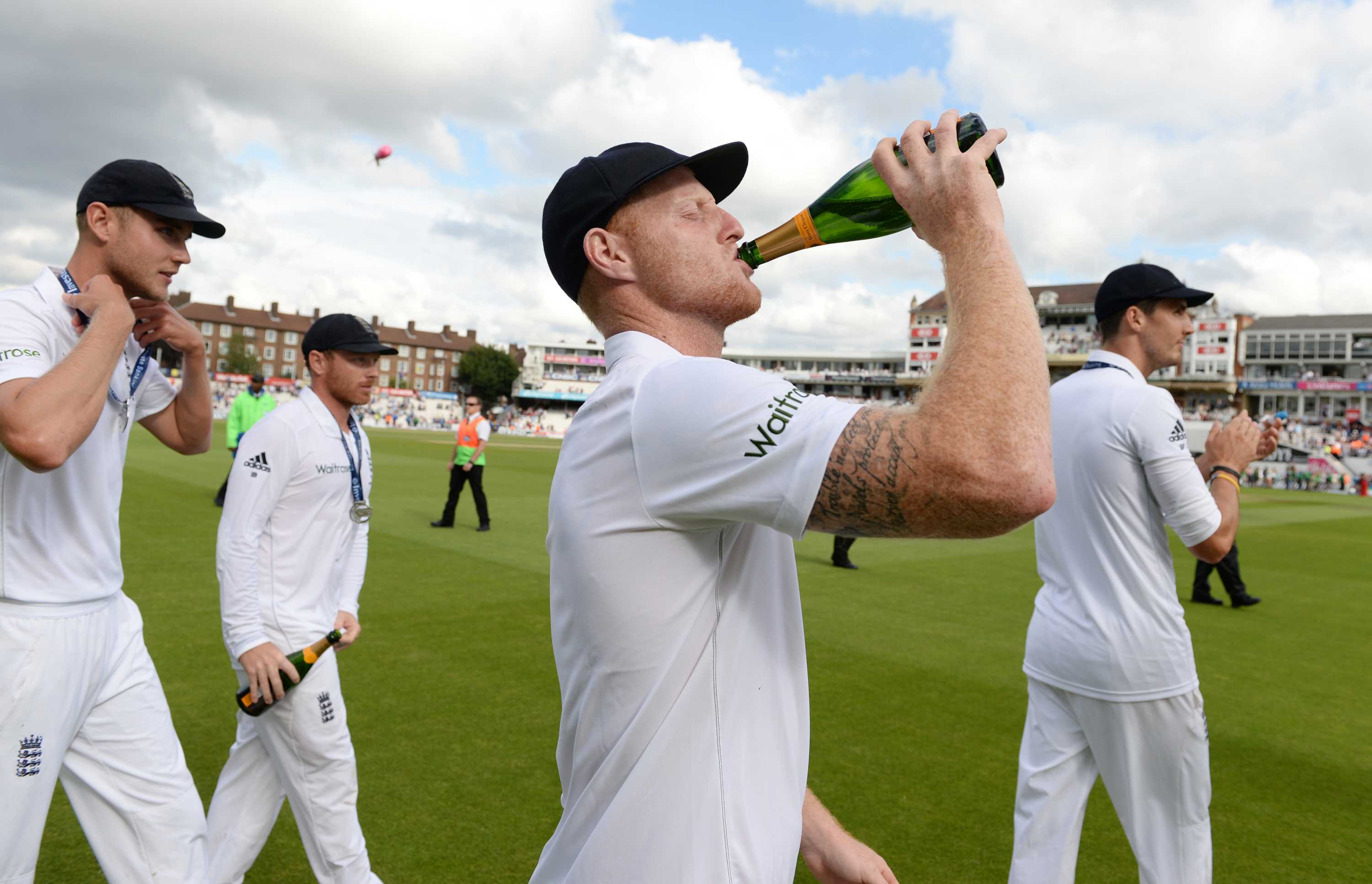 Ben Stokes, wearing his whites, swigs from a champagne bottle on the field.