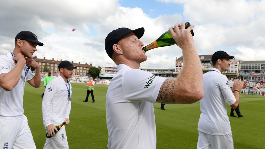 Ben Stokes, wearing his whites, swigs from a champagne bottle on the field.