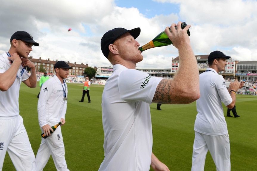 Ben Stokes, wearing his whites, swigs from a champagne bottle on the field.
