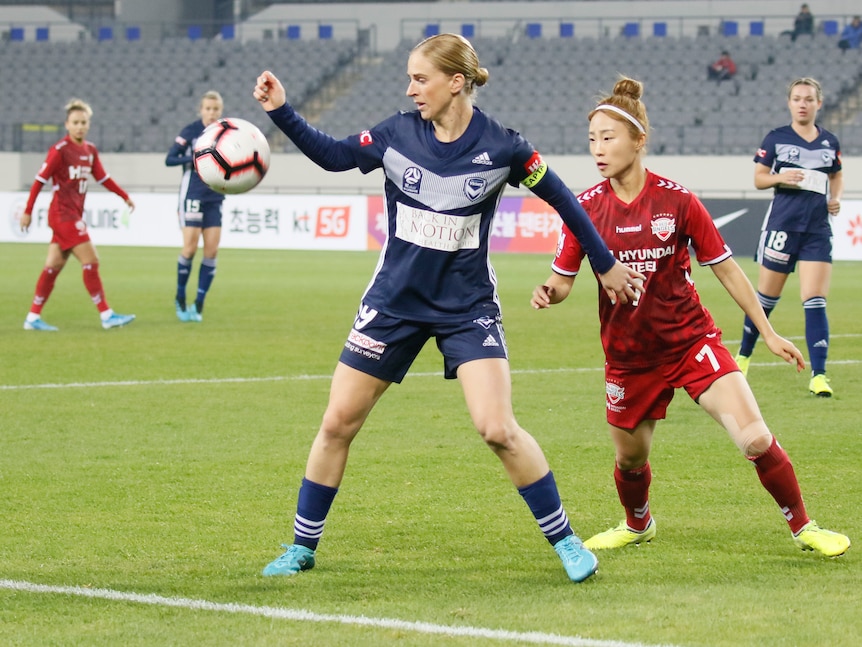 Two soccer players, one wearing dark blue and the other wearing red, compete for the ball during a game 