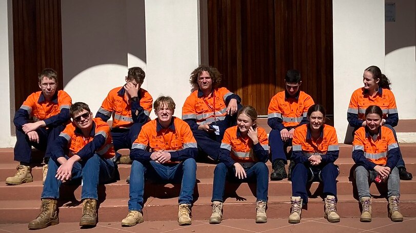 Students in high-vis sitting on the steps of a building.