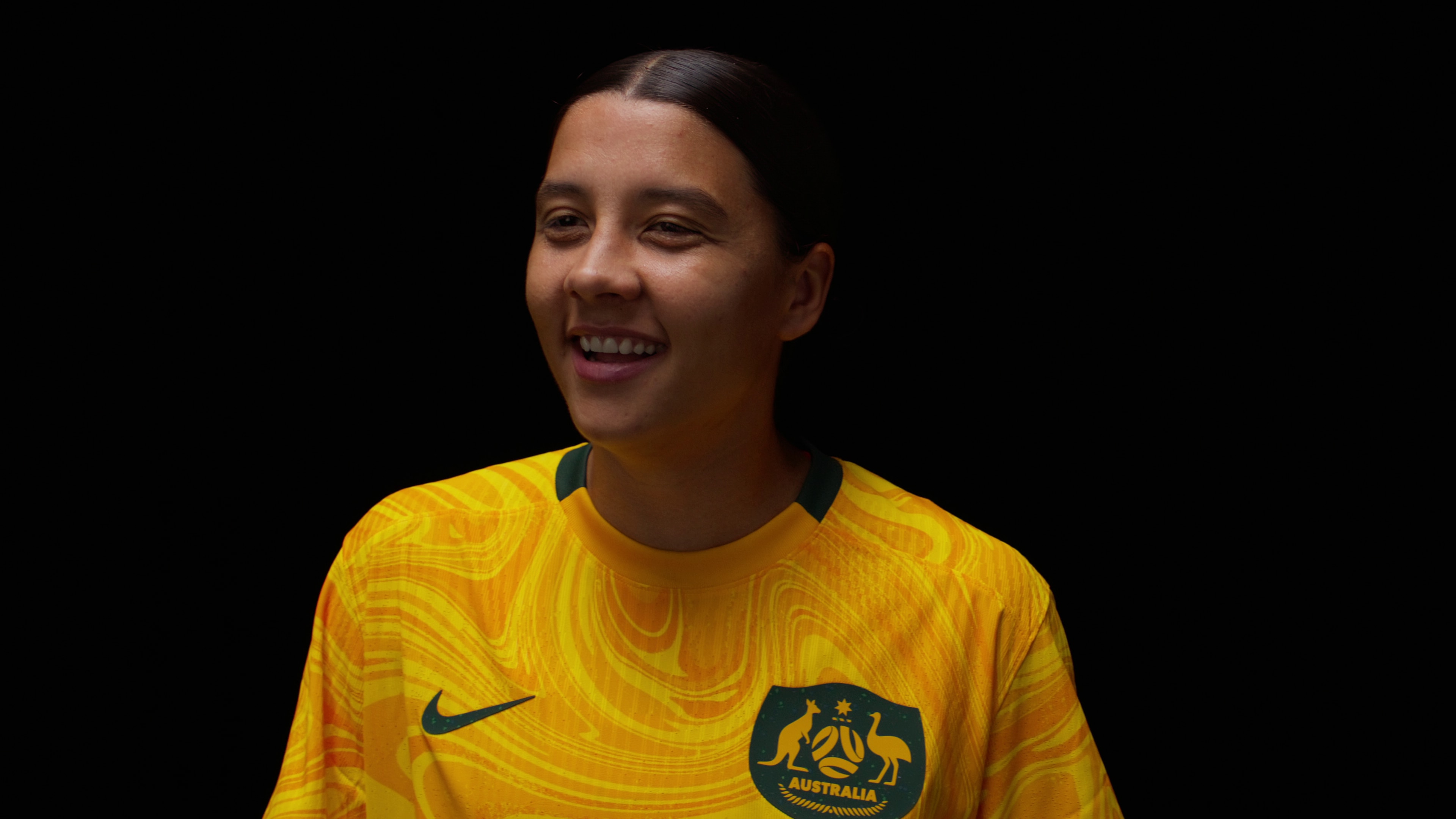 Sam laughs in her Matildas jersey against a black background.