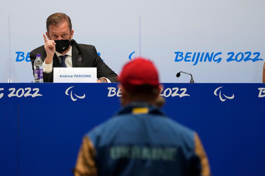 The IPC president Andrew Parsons gestures as he replies to a question from a journalist standing at a press conference.