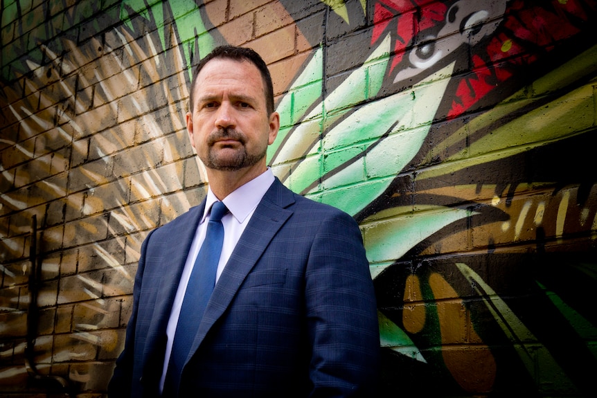 A man in a suit leaning against a wall.