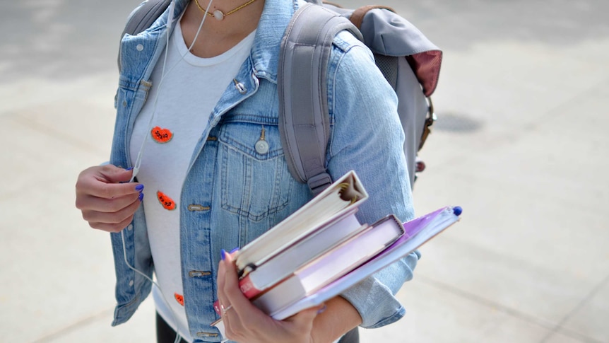 A student holding the wires of her headphones in one hand and books in another hand.