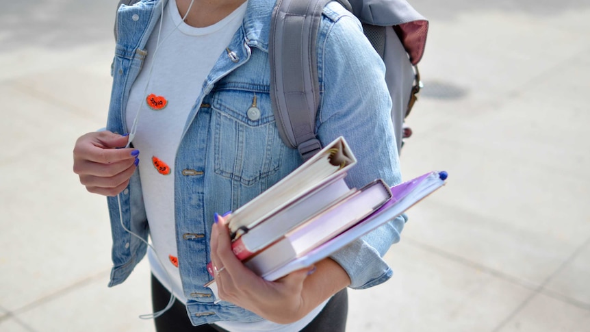 A university student carrying books while wearing headphones.