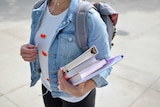 A university student carrying books while wearing headphones.
