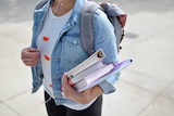 A student holding the wires of her headphones in one hand and books in another hand.