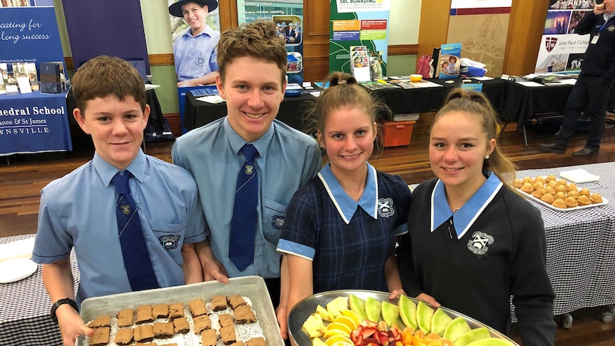 Four boarding school students (two boys, two girls) in uniform serving platters of fruit and biscuits at ICPA conference.