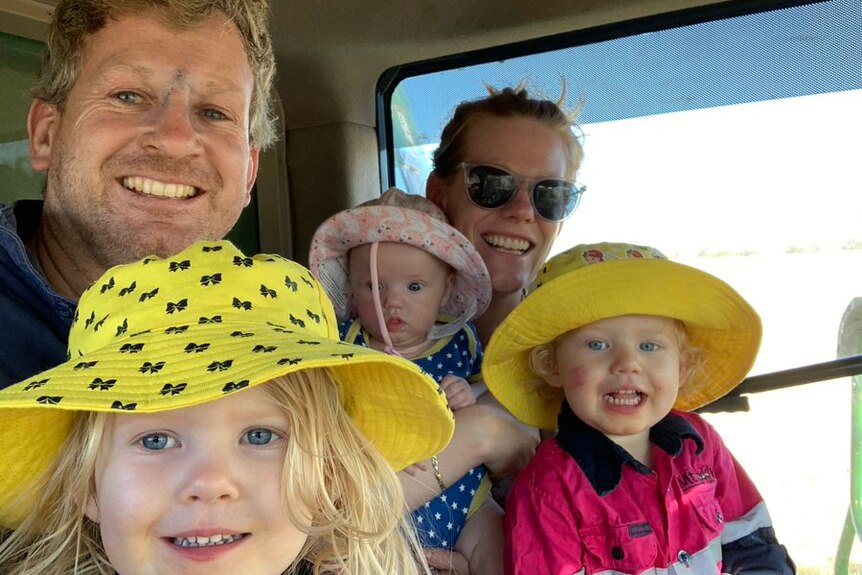 Family of five in a tractor cab, three little girls smiling in big hats.