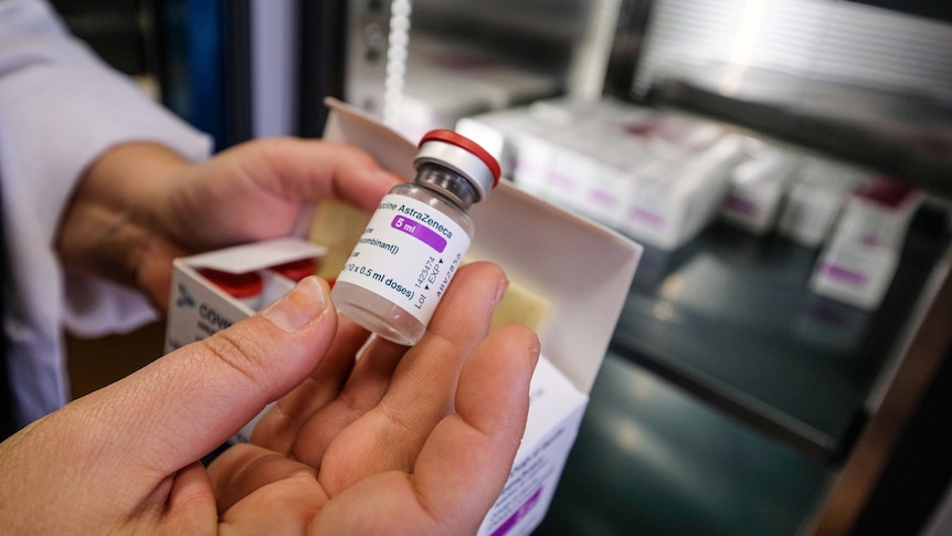 A hand holding a vaccine vial. AstraZeneca 5ml is printed on the label